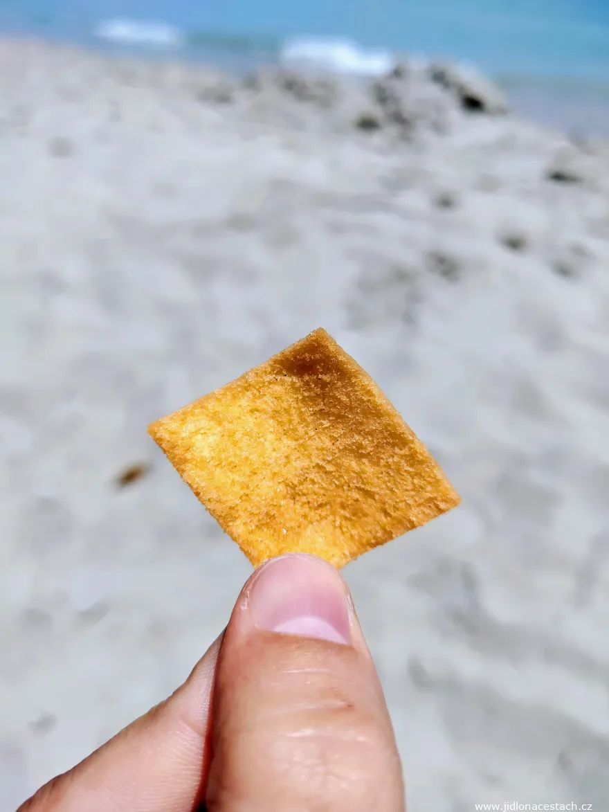 Un trozo cuadrado de pane guttiau entre los dedos, sobre la arena de la playa. Un trozo cuadrado de pane guttiau entre los dedos, sobre la arena de la playa.