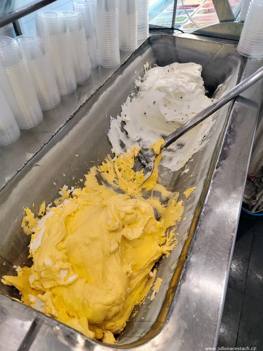Bastani sonnati au safran dans un grand bac réfrigéré. À gauche, on aperçoit les lamelles de crème gelée. L'autre glace du bac est une vanille aux pistaches entières.
