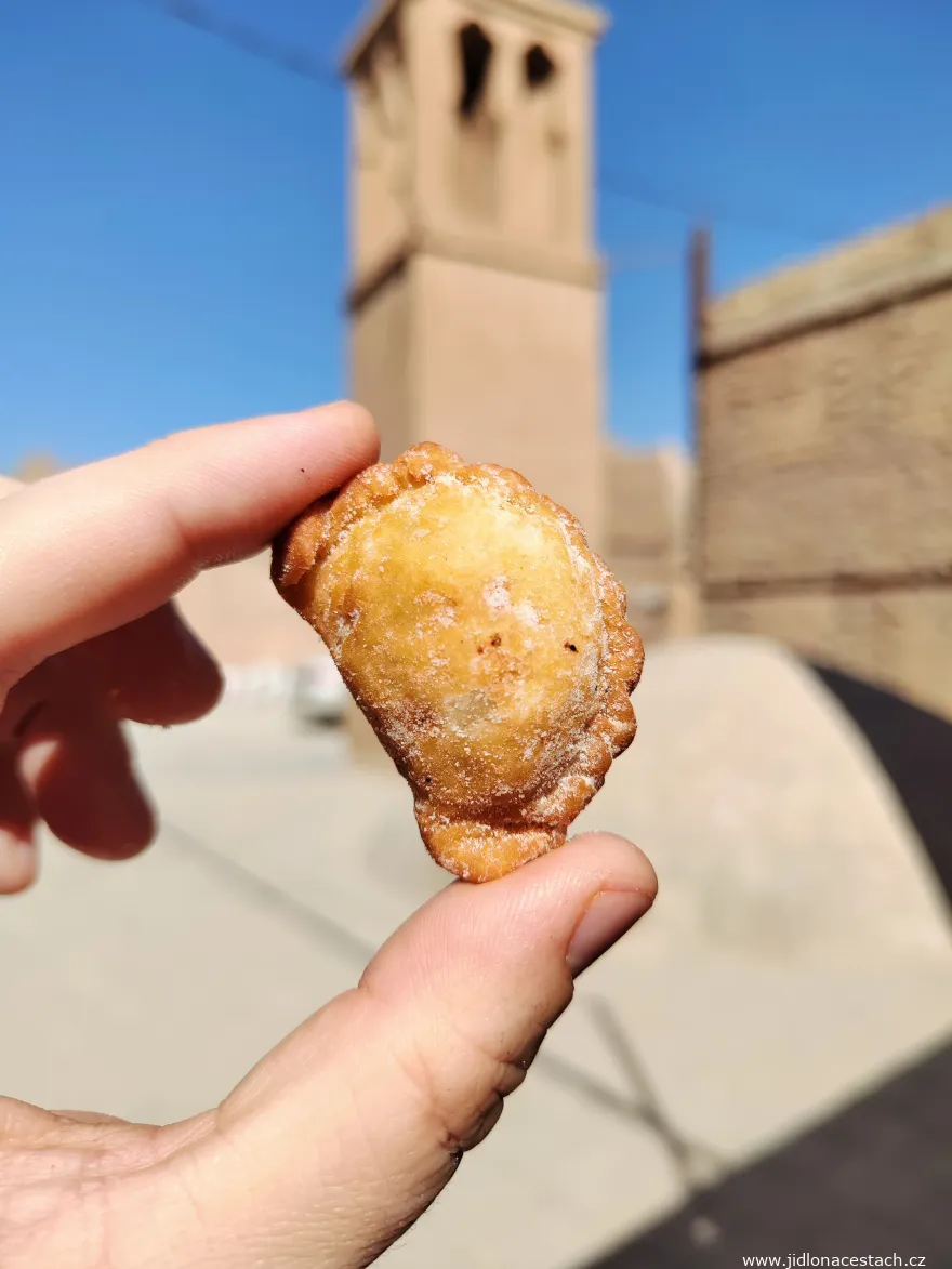 Qottab : pâtisserie iranienne sablée fourrée aux fruits secs, ici visiblement refermée en forme de chausson et roulée dans le sucre glace. En arrière-plan, l'une des nombreuses tours à vent de Yazd. Qottab : pâtisserie iranienne sablée fourrée aux fruits secs, ici visiblement refermée en forme de chausson et roulée dans le sucre glace. En arrière-plan, l'une des nombreuses tours à vent de Yazd.