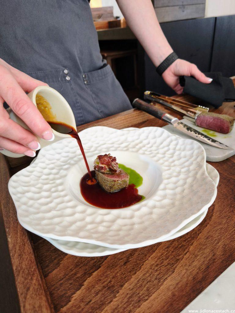 Field Restaurant: finishing and assembling the entire dish right before the guest. The fallow deer saddle is complemented by a slice of homemade dried pork neck and poured over with truffle jus. Roasted mushrooms with truffle vinaigrette, lovage foam, and mushroom chips are served as a side dish.